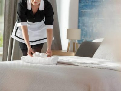 Young maid laying fresh towels on a bed in hotel room
