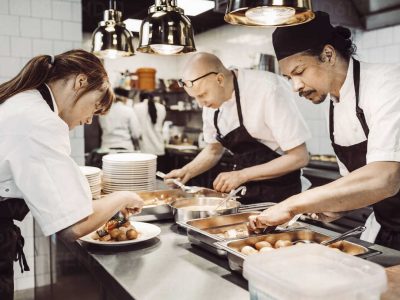 Kvinnlig sous chef och två manliga kockar förbereder maträtter